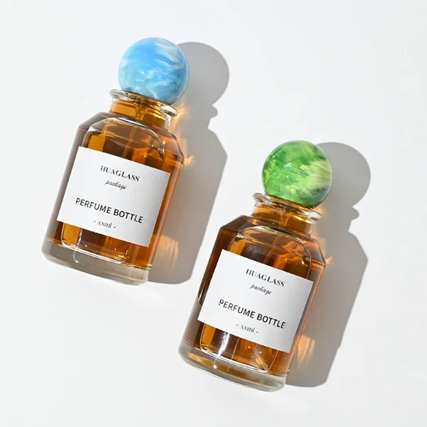 HUA0017 perfume bottle, heavy-base cylindrical round glass bottle with clear finish, featuring a square paper label and a large spherical plastic ball cap showcasing unique marbled veining patterns, elegant classic fragrance packaging design in 100ml