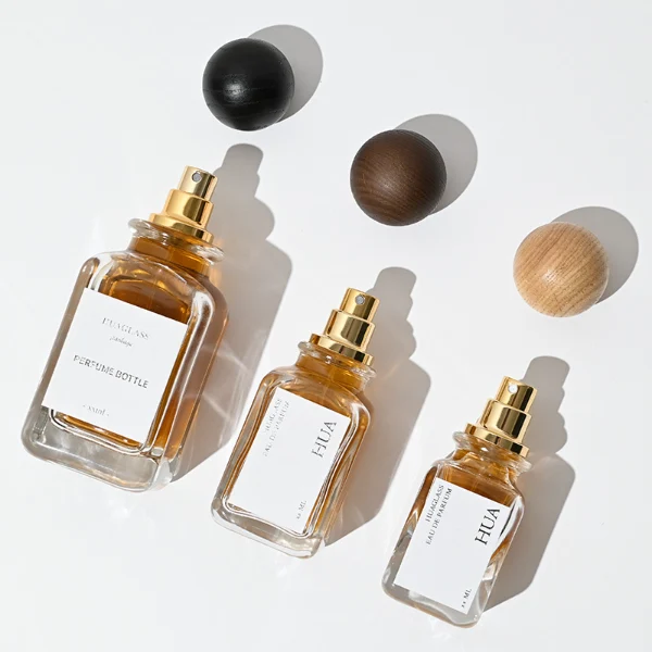 Smooth spherical wooden caps featuring distinct grain finishes in black, dark brown, and natural tones. Elegant square perfume bottles with rounded vertical edges crafted from clear glass filled with golden-amber liquid.