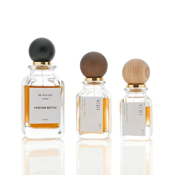 Smooth spherical wooden caps featuring distinct grain finishes in black, dark brown, and natural tones. Elegant square perfume bottles with rounded vertical edges crafted from clear glass filled with golden-amber liquid.