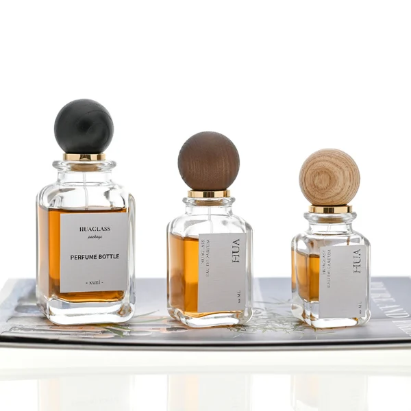Smooth spherical wooden caps featuring distinct grain finishes in black, dark brown, and natural tones. Elegant square perfume bottles with rounded vertical edges crafted from clear glass filled with golden-amber liquid.