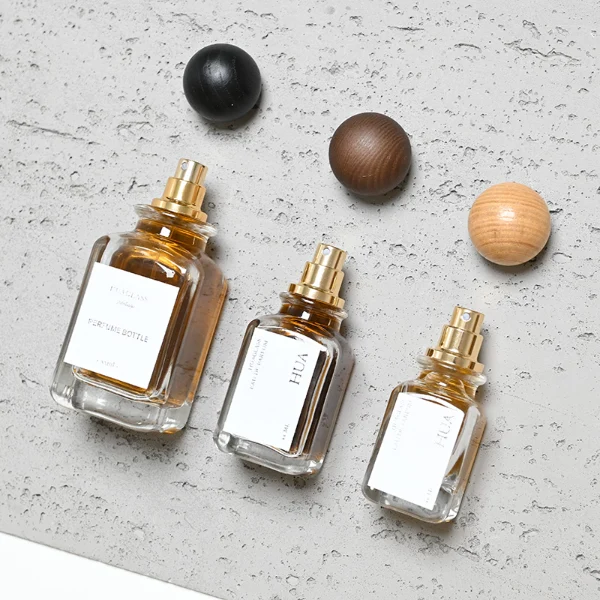 Smooth spherical wooden caps featuring distinct grain finishes in black, dark brown, and natural tones. Elegant square perfume bottles with rounded vertical edges crafted from clear glass filled with golden-amber liquid.