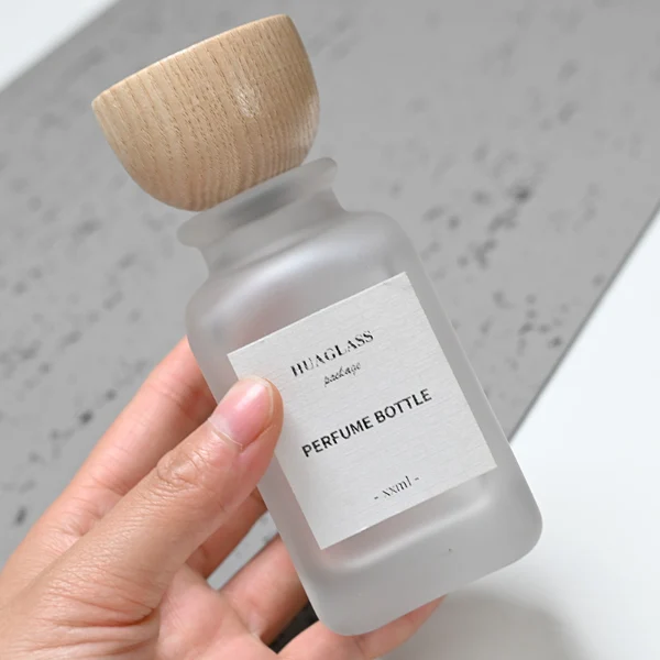HUA0041 perfume bottle, frosted clear or smoky grey gradient cylindrical round glass bottle featuring an eye-catching inverted conical cup-shaped wood cap with prominent natural wood grain lines, elegant modern fragrance packaging design available in 30ml, 50ml, and 100ml