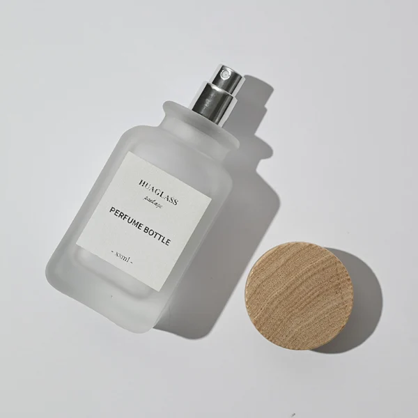 HUA0041 perfume bottle, frosted clear or smoky grey gradient cylindrical round glass bottle featuring an eye-catching inverted conical cup-shaped wood cap with prominent natural wood grain lines, elegant modern fragrance packaging design available in 30ml, 50ml, and 100ml