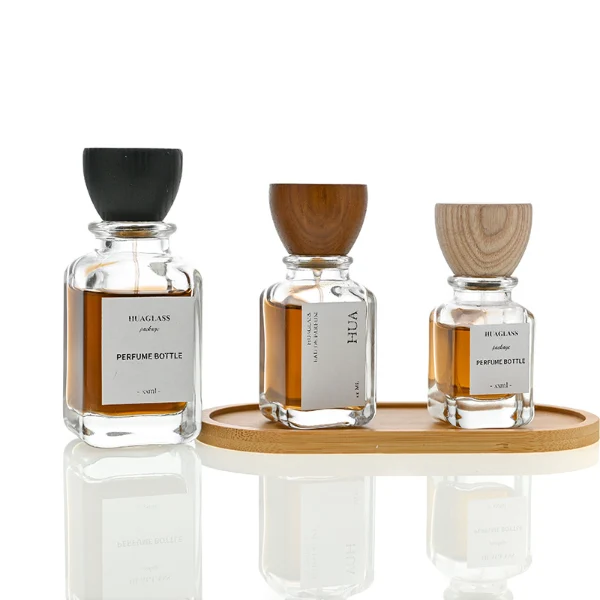 HUA0023 perfume bottle, heavy-base square cuboid glass bottle with clear finish and rounded edges, featuring a square paper label and an eye-catching inverted conical cup-shaped wood cap with prominent natural wood grain lines, elegant modern fragrance packaging design available in 30ml, 50ml, and 100ml