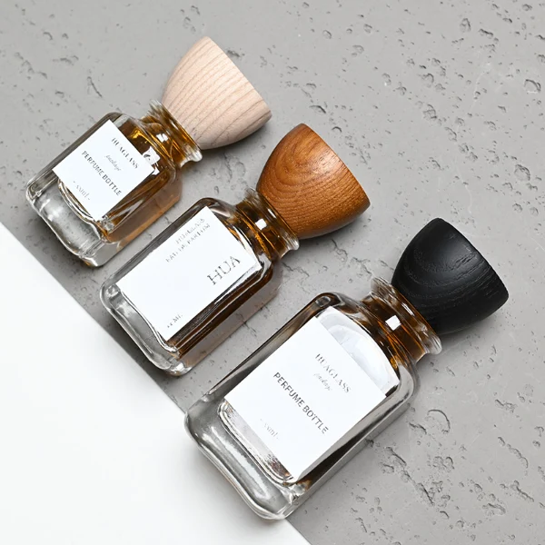 HUA0023 perfume bottle, heavy-base square cuboid glass bottle with clear finish and rounded edges, featuring a square paper label and an eye-catching inverted conical cup-shaped wood cap with prominent natural wood grain lines, elegant modern fragrance packaging design available in 30ml, 50ml, and 100ml