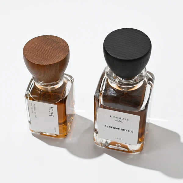 HUA0023 perfume bottle, heavy-base square cuboid glass bottle with clear finish and rounded edges, featuring a square paper label and an eye-catching inverted conical cup-shaped wood cap with prominent natural wood grain lines, elegant modern fragrance packaging design available in 30ml, 50ml, and 100ml