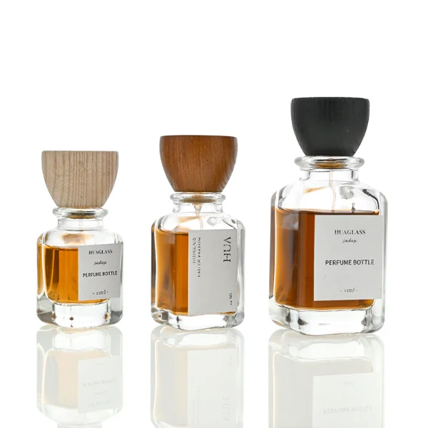 HUA0023 perfume bottle, heavy-base square cuboid glass bottle with clear finish and rounded edges, featuring a square paper label and an eye-catching inverted conical cup-shaped wood cap with prominent natural wood grain lines, elegant modern fragrance packaging design available in 30ml, 50ml, and 100ml