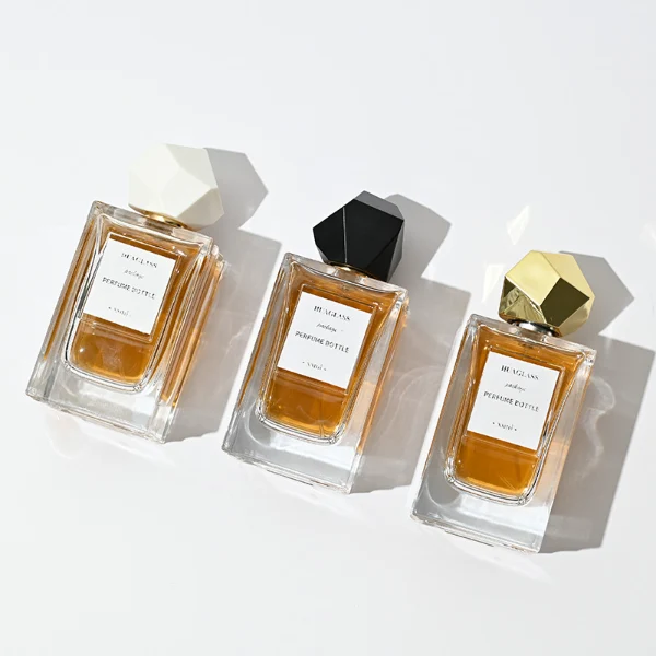HUA0025 perfume bottle, heavy-base square cuboid glass bottle with fluted side details and clear finish, featuring a square paper label and an eye-catching irregular multi-faceted rock-shaped plastic cap with a high-gloss shiny finish and sharp geometric angles, elegant modern fragrance packaging design available in 50ml and 100ml