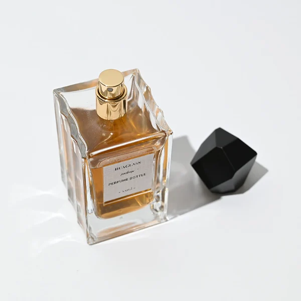 HUA0025 perfume bottle, heavy-base square cuboid glass bottle with fluted side details and clear finish, featuring a square paper label and an eye-catching irregular multi-faceted rock-shaped plastic cap with a high-gloss shiny finish and sharp geometric angles, elegant modern fragrance packaging design available in 50ml and 100ml