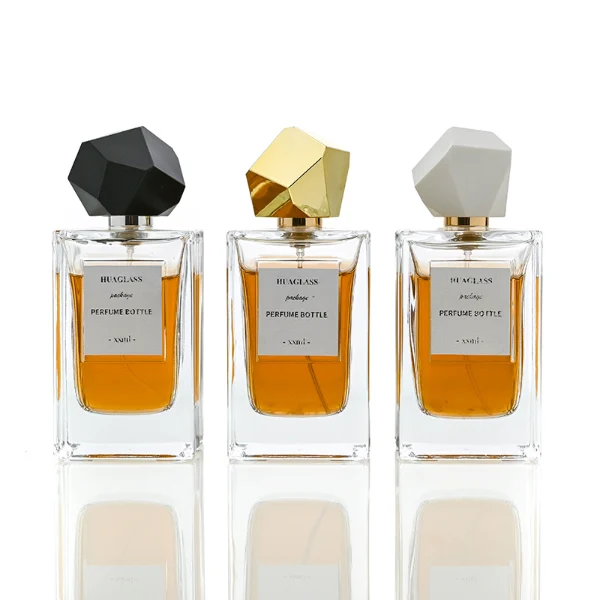 HUA0025 perfume bottle, heavy-base square cuboid glass bottle with fluted side details and clear finish, featuring a square paper label and an eye-catching irregular multi-faceted rock-shaped plastic cap with a high-gloss shiny finish and sharp geometric angles, elegant modern fragrance packaging design available in 50ml and 100ml