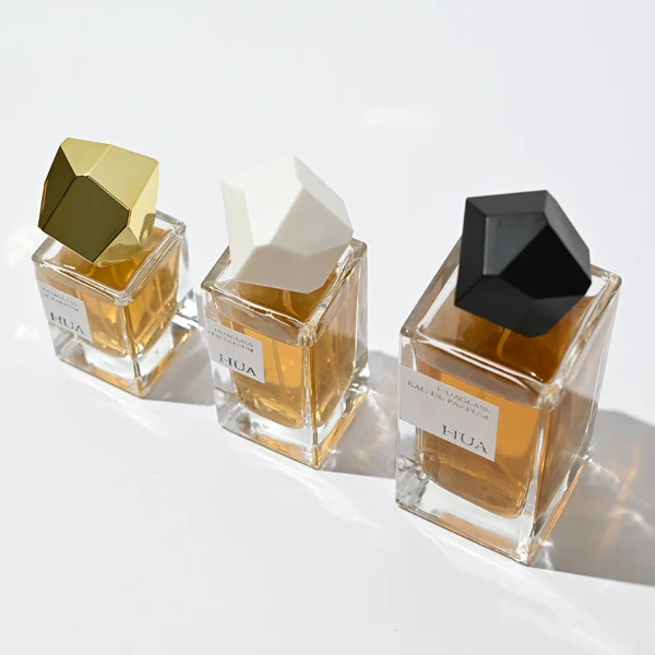 HUA0019 perfume bottle, heavy-base square cuboid glass bottle with clear finish, featuring a rectangular paper label and an eye-catching irregular multi-faceted rock-shaped plastic cap with a high-gloss white finish, elegant modern fragrance packaging design available in 30ml, 50ml, and 100ml