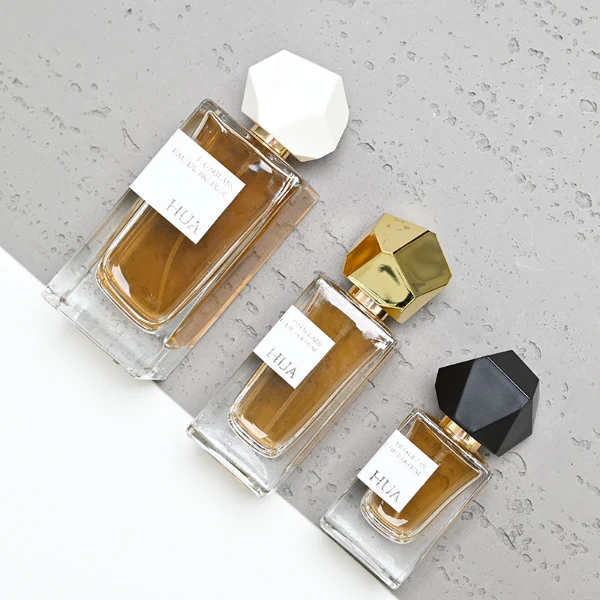 HUA0019 perfume bottle, heavy-base square cuboid glass bottle with clear finish, featuring a rectangular paper label and an eye-catching irregular multi-faceted rock-shaped plastic cap with a high-gloss white finish, elegant modern fragrance packaging design available in 30ml, 50ml, and 100ml