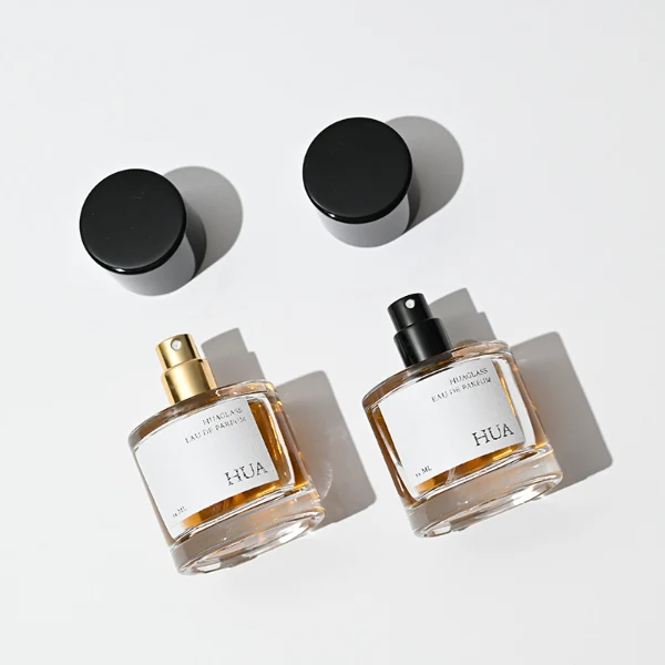 HUA0018 perfume bottle, heavy-base cylindrical round glass bottle with clear finish, featuring a rectangular paper label and a tall cylindrical plastic cap with a high-gloss black finish, elegant modern fragrance packaging design available in 30ml, 50ml, and 100ml