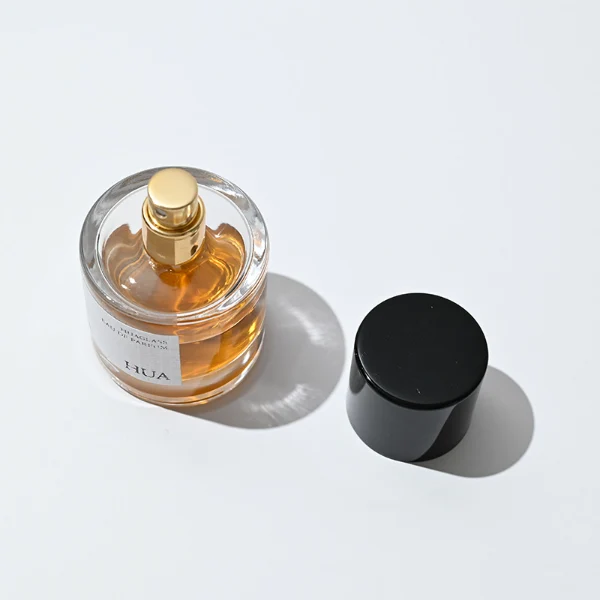 HUA0018 perfume bottle, heavy-base cylindrical round glass bottle with clear finish, featuring a rectangular paper label and a tall cylindrical plastic cap with a high-gloss black finish, elegant modern fragrance packaging design available in 30ml, 50ml, and 100ml