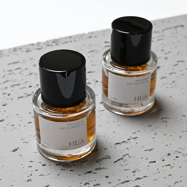 HUA0018 perfume bottle, heavy-base cylindrical round glass bottle with clear finish, featuring a rectangular paper label and a tall cylindrical plastic cap with a high-gloss black finish, elegant modern fragrance packaging design available in 30ml, 50ml, and 100ml