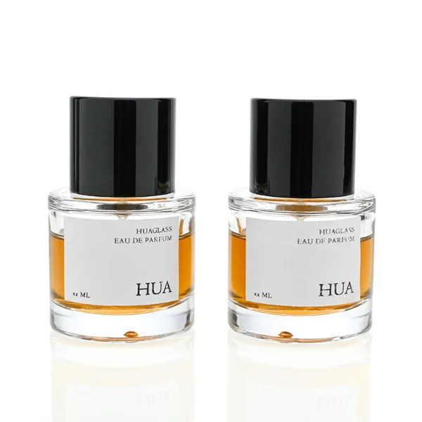 HUA0018 perfume bottle, heavy-base cylindrical round glass bottle with clear finish, featuring a rectangular paper label and a tall cylindrical plastic cap with a high-gloss black finish, elegant modern fragrance packaging design available in 30ml, 50ml, and 100ml