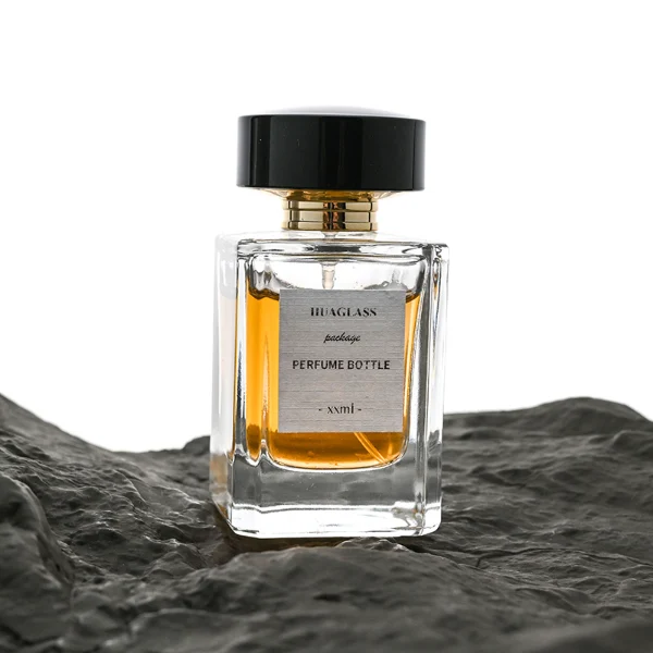 HUA0027 perfume bottle, heavy-base rectangular cuboid glass bottle with clear finish, featuring a square paper label, a polished gold neck, and a wide cylindrical plastic cap with a smooth high-gloss shiny black finish, elegant modern fragrance packaging design available in 30ml, 50ml, and 100ml