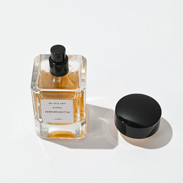HUA0027 perfume bottle, heavy-base rectangular cuboid glass bottle with clear finish, featuring a square paper label, a polished gold neck, and a wide cylindrical plastic cap with a smooth high-gloss shiny black finish, elegant modern fragrance packaging design available in 30ml, 50ml, and 100ml