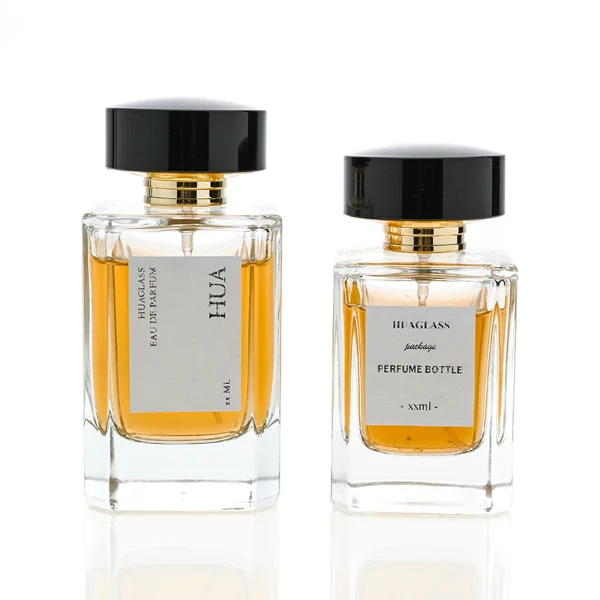 HUA0027 perfume bottle, heavy-base rectangular cuboid glass bottle with clear finish, featuring a square paper label, a polished gold neck, and a wide cylindrical plastic cap with a smooth high-gloss shiny black finish, elegant modern fragrance packaging design available in 30ml, 50ml, and 100ml