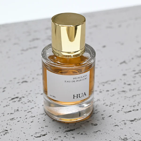 HUA0045 perfume bottle, heavy-base cylindrical round glass bottle with clear finish, featuring a square paper label, a coordinating collar neck accent, and a tall cylindrical aluminum cap with a smooth polished metallic finish, elegant modern fragrance packaging design available in 30ml, 50ml, and 100ml