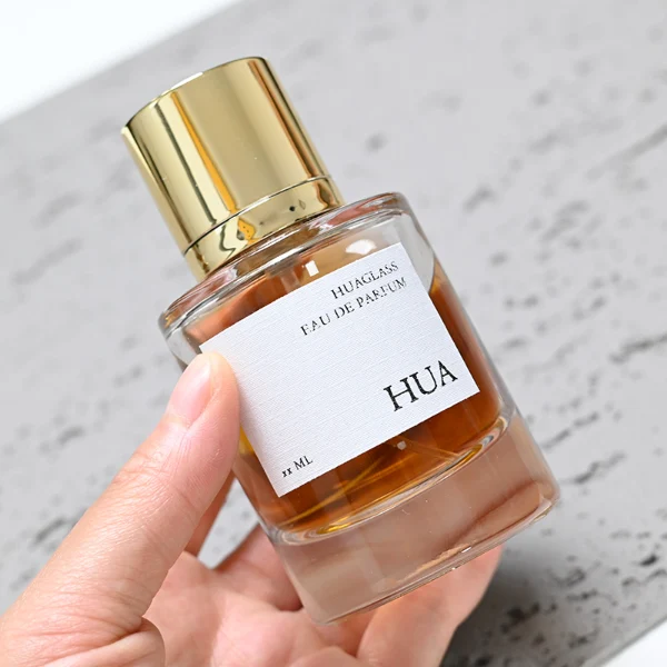 HUA0045 perfume bottle, heavy-base cylindrical round glass bottle with clear finish, featuring a square paper label, a coordinating collar neck accent, and a tall cylindrical aluminum cap with a smooth polished metallic finish, elegant modern fragrance packaging design available in 30ml, 50ml, and 100ml
