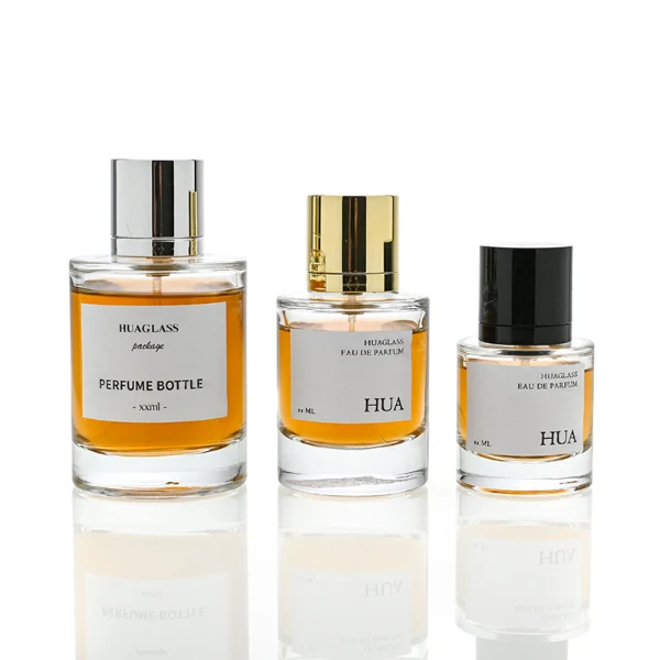 HUA0045 perfume bottle, heavy-base cylindrical round glass bottle with clear finish, featuring a square paper label, a coordinating collar neck accent, and a tall cylindrical aluminum cap with a smooth polished metallic finish, elegant modern fragrance packaging design available in 30ml, 50ml, and 100ml