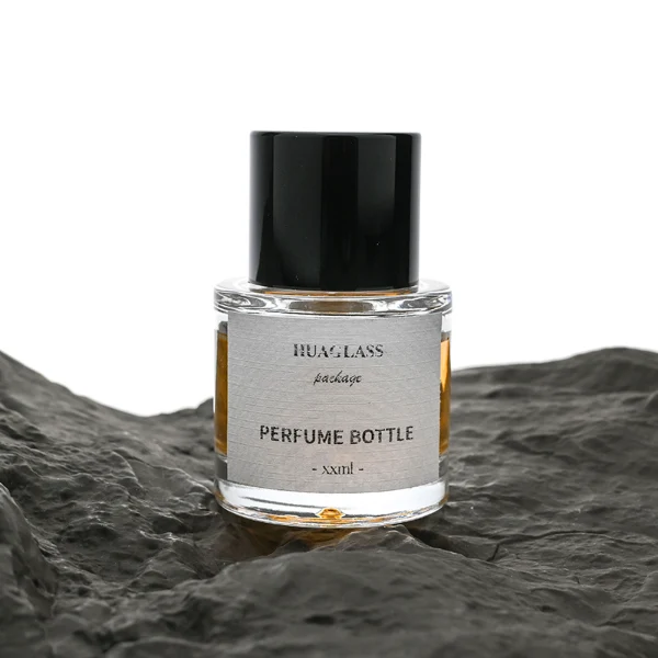 HUA0047 perfume bottle, heavy-base cylindrical round glass bottle with clear finish, featuring a square paper label and a wide cylindrical solid black plastic cap with a smooth high-gloss shiny finish, elegant modern fragrance packaging design available in 30ml, 50ml, and 100ml