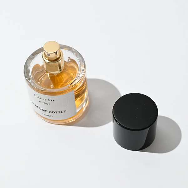 HUA0047 perfume bottle, heavy-base cylindrical round glass bottle with clear finish, featuring a square paper label and a wide cylindrical solid black plastic cap with a smooth high-gloss shiny finish, elegant modern fragrance packaging design available in 30ml, 50ml, and 100ml