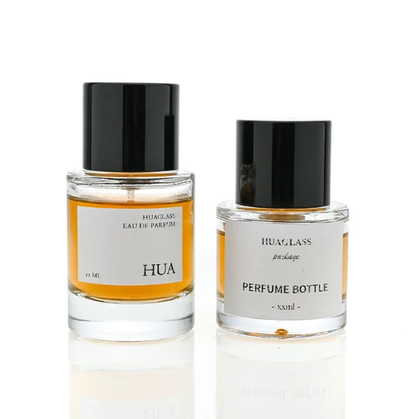 HUA0047 perfume bottle, heavy-base cylindrical round glass bottle with clear finish, featuring a square paper label and a wide cylindrical solid black plastic cap with a smooth high-gloss shiny finish, elegant modern fragrance packaging design available in 30ml, 50ml, and 100ml