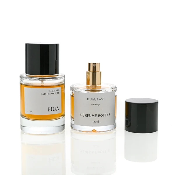 HUA0047 perfume bottle, heavy-base cylindrical round glass bottle with clear finish, featuring a square paper label and a wide cylindrical solid black plastic cap with a smooth high-gloss shiny finish, elegant modern fragrance packaging design available in 30ml, 50ml, and 100ml