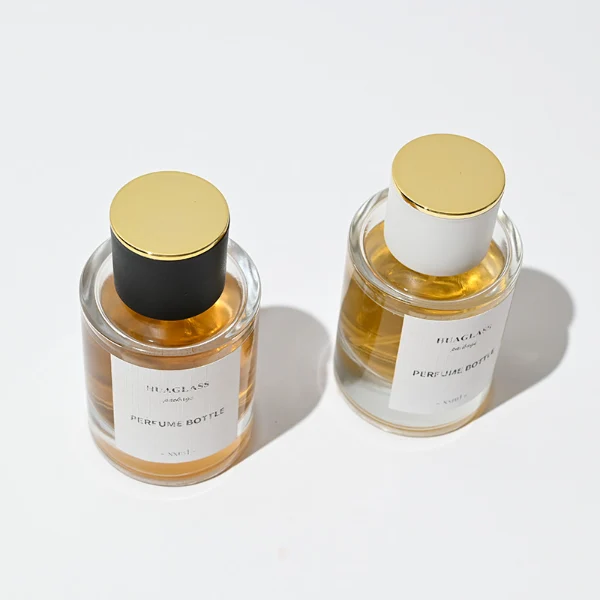 HUA0037 perfume bottle, heavy-base cylindrical round glass bottle with clear finish, featuring a square paper label, a metallic gold collar neck accent, and a short cylindrical plastic cap with a smooth high-gloss shiny finish, elegant modern fragrance packaging design available in 30ml, 50ml, and 100ml