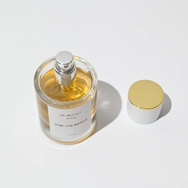HUA0037 perfume bottle, heavy-base cylindrical round glass bottle with clear finish, featuring a square paper label, a metallic gold collar neck accent, and a short cylindrical plastic cap with a smooth high-gloss shiny finish, elegant modern fragrance packaging design available in 30ml, 50ml, and 100ml