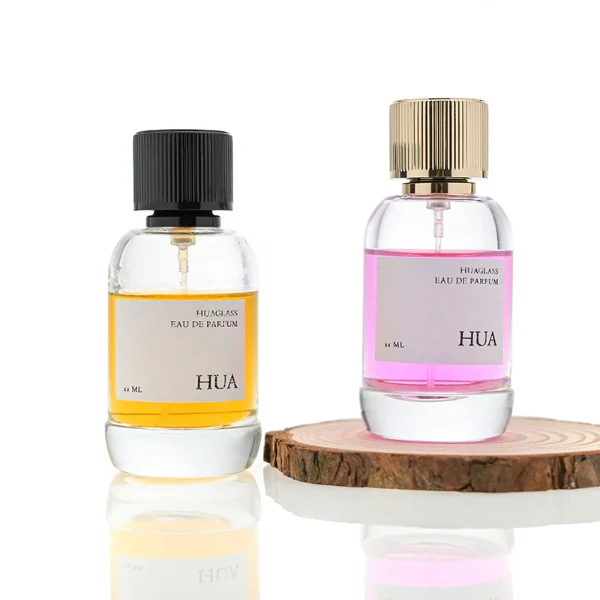 HUA0055 perfume bottle, heavy-base cylindrical round glass bottle with clear finish, featuring a square paper label, a matching neck, and a tall vertically ribbed cylindrical aluminum cap with a smooth polished finish, elegant modern fragrance packaging design available in 30ml, 50ml, and 100ml