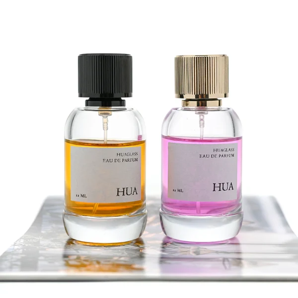 HUA0055 perfume bottle, heavy-base cylindrical round glass bottle with clear finish, featuring a square paper label, a matching neck, and a tall vertically ribbed cylindrical aluminum cap with a smooth polished finish, elegant modern fragrance packaging design available in 30ml, 50ml, and 100ml