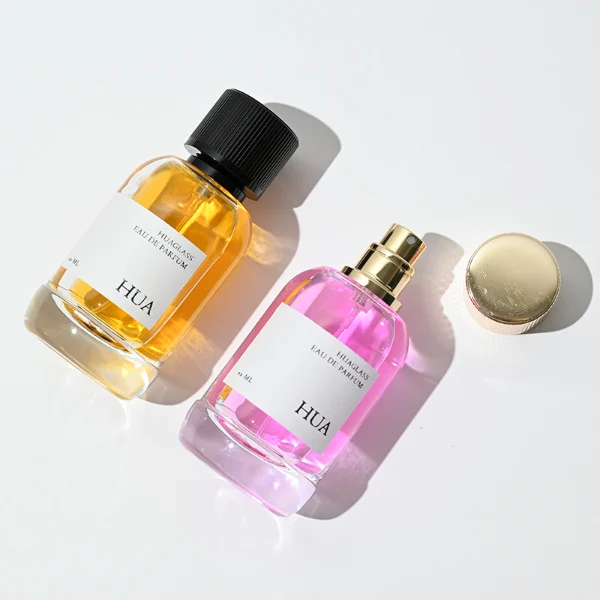 HUA0055 perfume bottle, heavy-base cylindrical round glass bottle with clear finish, featuring a square paper label, a matching neck, and a tall vertically ribbed cylindrical aluminum cap with a smooth polished finish, elegant modern fragrance packaging design available in 30ml, 50ml, and 100ml