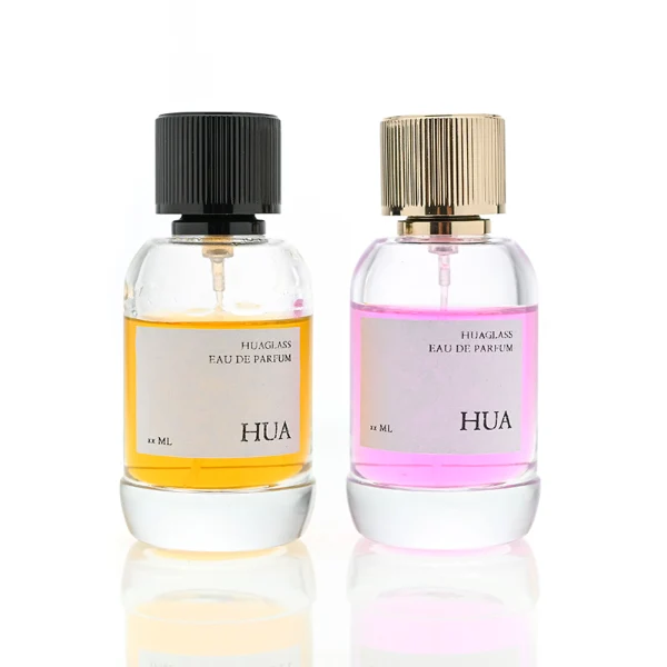 HUA0055 perfume bottle, heavy-base cylindrical round glass bottle with clear finish, featuring a square paper label, a matching neck, and a tall vertically ribbed cylindrical aluminum cap with a smooth polished finish, elegant modern fragrance packaging design available in 30ml, 50ml, and 100ml