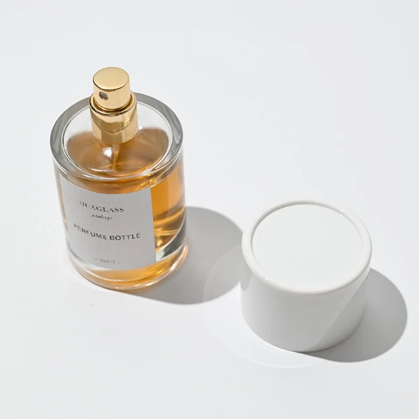 HUA0021 perfume bottle, heavy-base cylindrical round glass bottle with clear finish, featuring a square paper label, a matching neck, and a tall cylindrical plastic cap with a smooth high-gloss shiny finish, elegant modern fragrance packaging design available in 30ml, 50ml, and 100ml