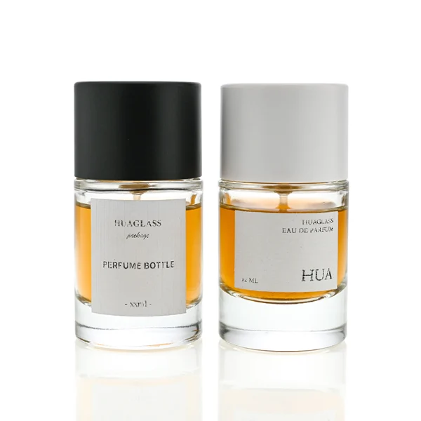 HUA0021 perfume bottle, heavy-base cylindrical round glass bottle with clear finish, featuring a square paper label, a matching neck, and a tall cylindrical plastic cap with a smooth high-gloss shiny finish, elegant modern fragrance packaging design available in 30ml, 50ml, and 100ml