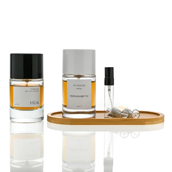 HUA0021 perfume bottle, heavy-base cylindrical round glass bottle with clear finish, featuring a square paper label, a matching neck, and a tall cylindrical plastic cap with a smooth high-gloss shiny finish, elegant modern fragrance packaging design available in 30ml, 50ml, and 100ml
