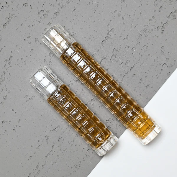 HUA0046 perfume bottle, tall slender cylindrical column glass bottle with clear finish and stacked grid-like textured ridges, featuring a gold collar neck accent and a matching tall transparent cylindrical plastic cap with a high-gloss shiny finish, modern geometric fragrance packaging design available in 30ml and 50ml