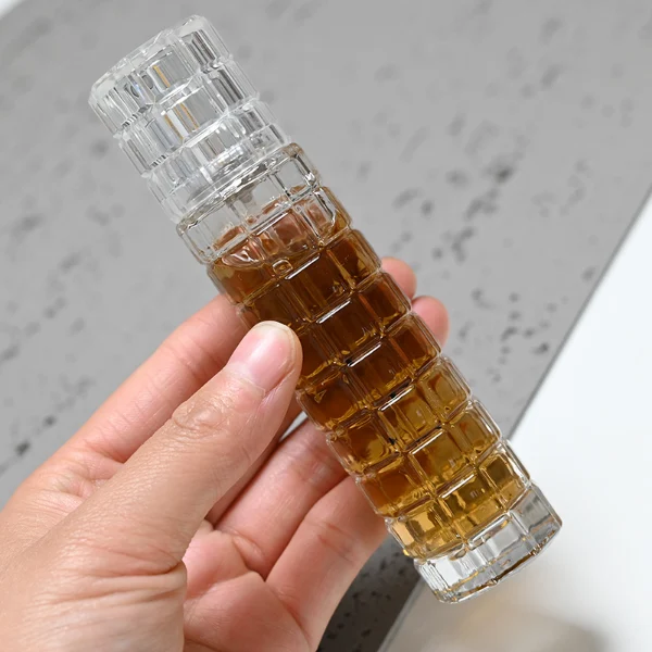 HUA0046 perfume bottle, tall slender cylindrical column glass bottle with clear finish and stacked grid-like textured ridges, featuring a gold collar neck accent and a matching tall transparent cylindrical plastic cap with a high-gloss shiny finish, modern geometric fragrance packaging design available in 30ml and 50ml