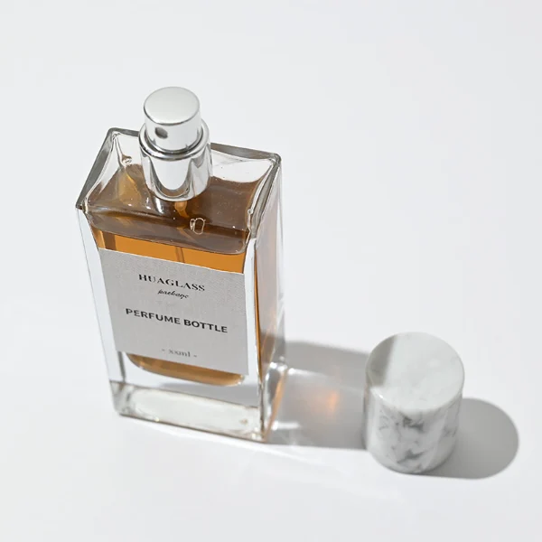 HUA0001 perfume bottle, heavy-base rectangular cuboid glass bottle with clear finish, featuring a square paper label, a matching neck, and a tall cylindrical synthetic polymer cap with an organic marbled or solid glossy finish, elegant modern fragrance packaging design available in 30ml, 50ml, and 100ml
