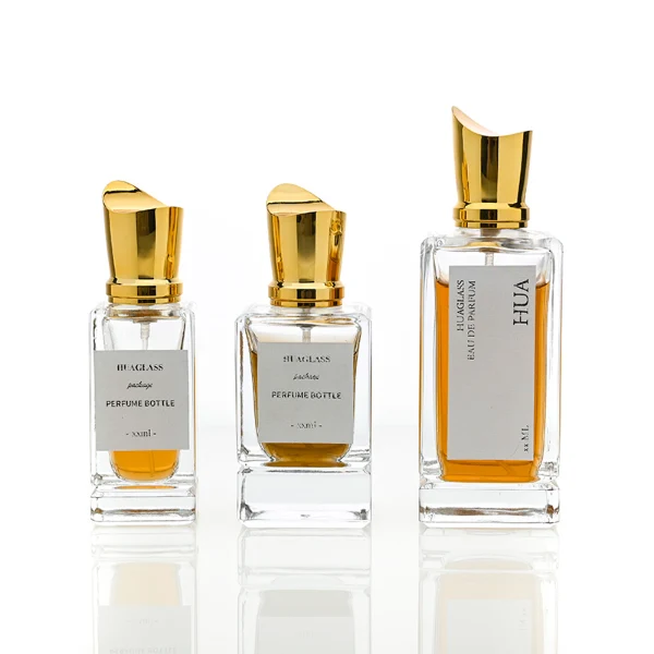 HUA0058 perfume bottle, heavy-base rectangular cuboid glass bottle with clear finish, featuring a paper label, a matching neck, and a tall sculptural cylindrical plastic cap with a sharply angled sloping top in a smooth high-gloss shiny gold finish, elegant modern fragrance packaging design available in 30ml, 50ml, and 100ml