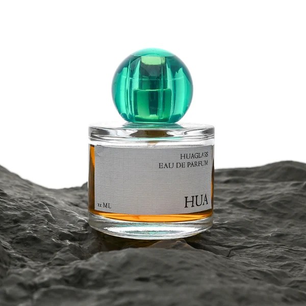 HUA0028 perfume bottle, transparent colorless rounded cylindrical glass body with thick base and smooth curved shoulder, 100 ml liquid, spherical transparent plastic cap with visible inner spray structure in green or clear color, brand label attached on bottle surface, modern elegant luxury design, ideal for gifting and daily use.