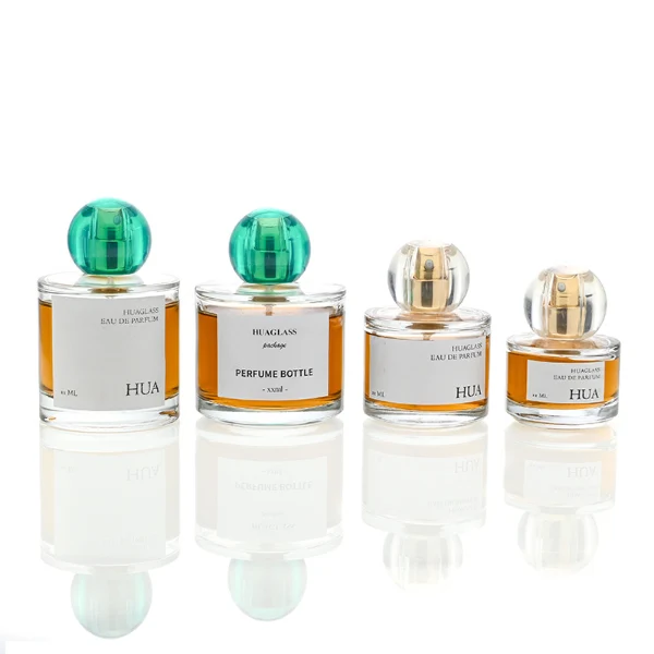 HUA0028 perfume bottle, transparent colorless rounded cylindrical glass body with thick base and smooth curved shoulder, 100 ml liquid, spherical transparent plastic cap with visible inner spray structure in green or clear color, brand label attached on bottle surface, modern elegant luxury design, ideal for gifting and daily use.