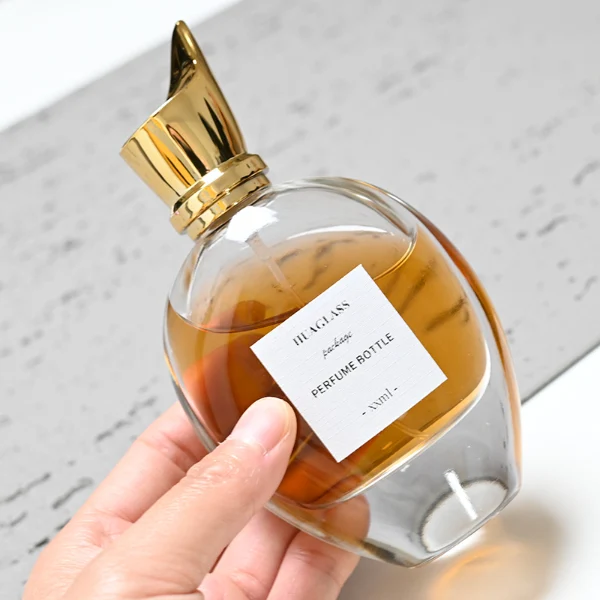 HUA0059 perfume bottle, heavy-base oval teardrop glass bottle with clear finish, featuring a square paper label, a matching neck, and a tall sculptural cylindrical plastic cap with a sharply angled sloping top in a smooth high-gloss shiny finish, elegant modern fragrance packaging design available in 30ml, 50ml, 75ml, and 100m