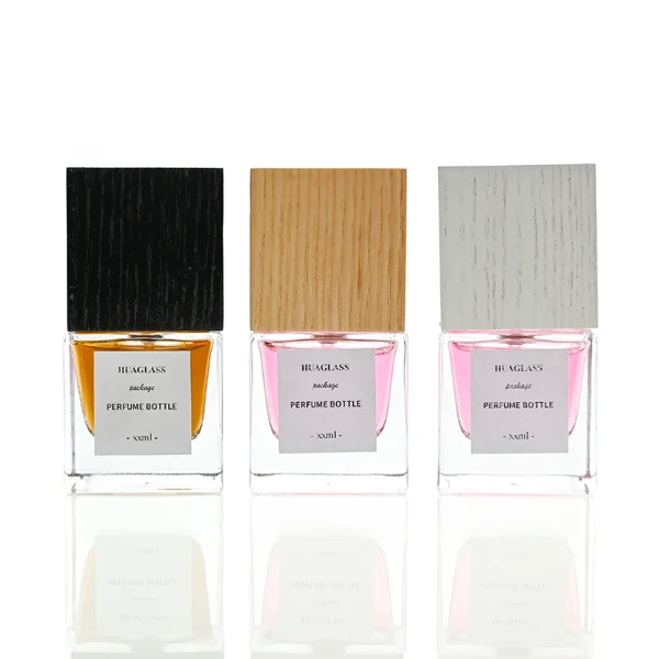 HUA0007 perfume bottle, luxury heavy-base square cuboid glass bottle with high-transparency clear finish, featuring a square paper label and a prominent tall flush-fit square natural textured wooden cap showcasing deep vertical wood grains, minimalist elegant fragrance packaging design available in 30ml, 50ml, and 100ml