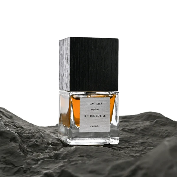 HUA0007 perfume bottle, luxury heavy-base square cuboid glass bottle with high-transparency clear finish, featuring a square paper label and a prominent tall flush-fit square natural textured wooden cap showcasing deep vertical wood grains, minimalist elegant fragrance packaging design available in 30ml, 50ml, and 100ml