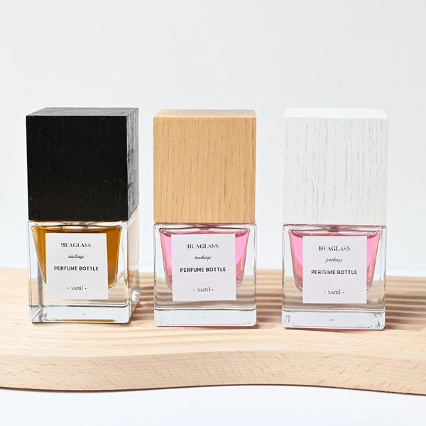 HUA0007 perfume bottle, luxury heavy-base square cuboid glass bottle with high-transparency clear finish, featuring a square paper label and a prominent tall flush-fit square natural textured wooden cap showcasing deep vertical wood grains, minimalist elegant fragrance packaging design available in 30ml, 50ml, and 100ml
