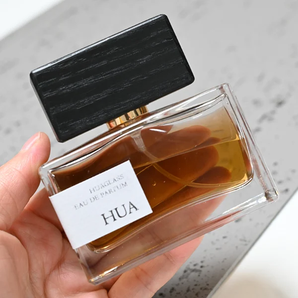 HUA0036 perfume bottle, heavy-base wide rectangular cuboid glass bottle with clear finish, featuring a side-set paper label, a metallic gold collar neck accent, and a prominent wide rectangular block-shaped wood cap with prominent natural wood grain lines, elegant modern fragrance packaging design available in 30ml, 50ml, and 100ml